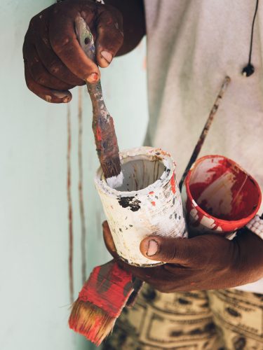 Serge Toussaint dips a brush into some paint as he works on one of his murals in Little Haiti, Miami, FL.