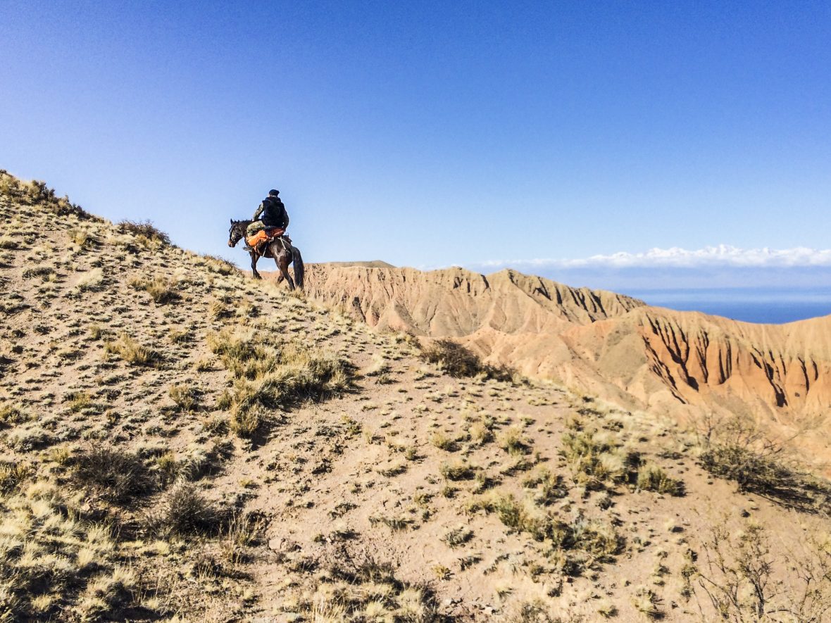 A man on horseback climbs steep hills of Kyrgyzstan