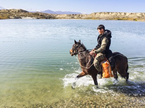 Man rides horse through water in Kyrgyzstan