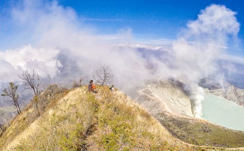 A woman on a mountain with blue skies and clouds around. Adventure Academy.