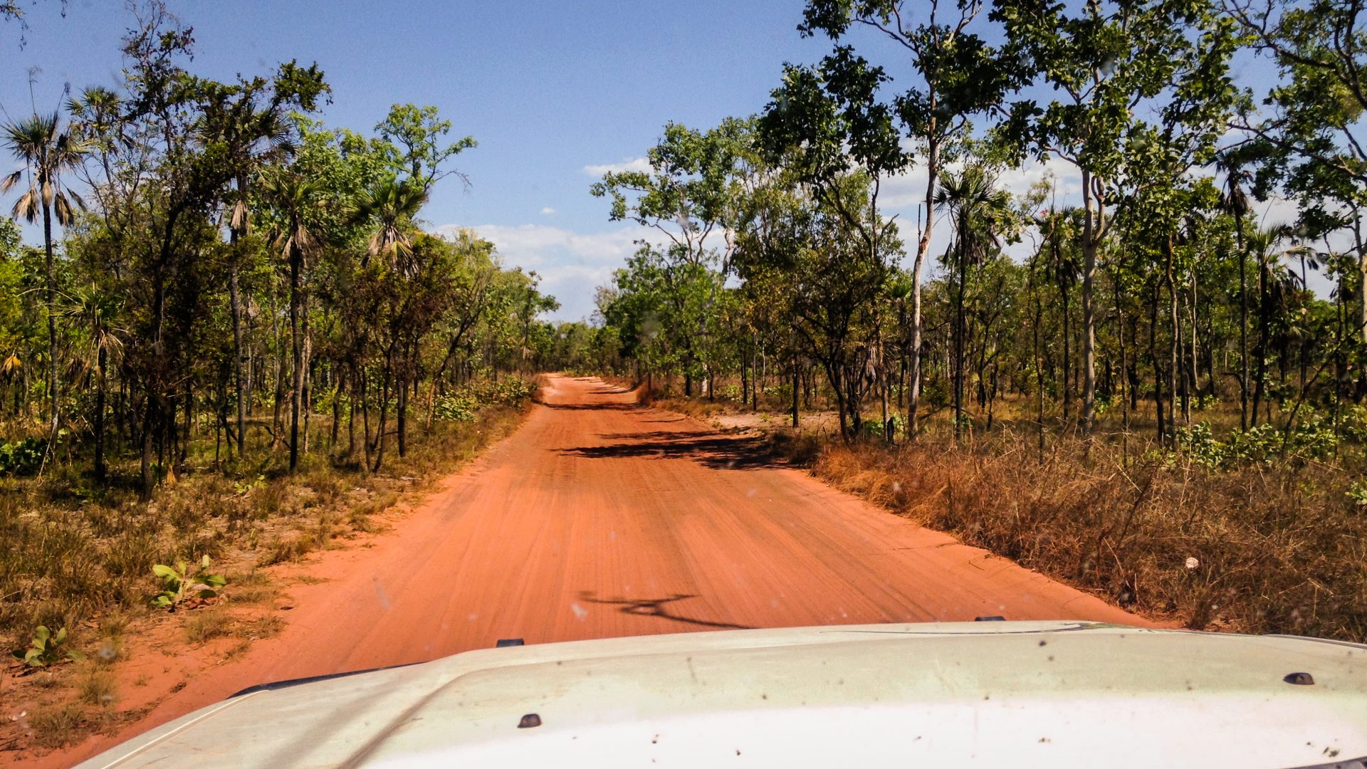 A jeep drives along a red road in the Australian Outback.