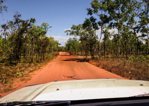 A jeep drives along a red road in the Australian Outback.