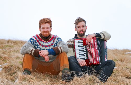 Men sit with an accordion on a hill in Iceland