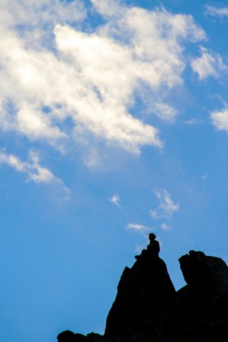 The silhouette of a person sits upon a cliff in the Indus Valley, Laddakh