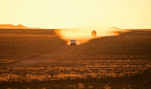 Hitchhiking Australi: A car leaves a trail of yellow dust at dusk in the outback.