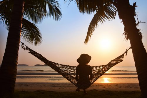 Silhouette of woman in hat sitting in hammock at sunset on the beach: solo travel