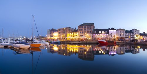A tranquil scene of Plymouth Barbican captured at twilight.The image shows the harbour with bars and restaurants at the waters edge.
