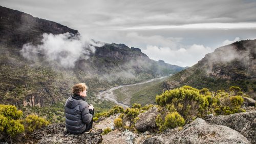 A traveler admires the mountainous vista during the Kilimanjaro hike, Tanzania.