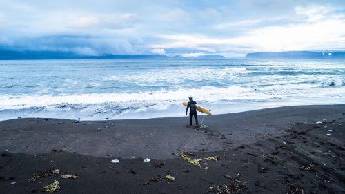 A surfer on the black sand beach in Bolungarvik, Iceland.