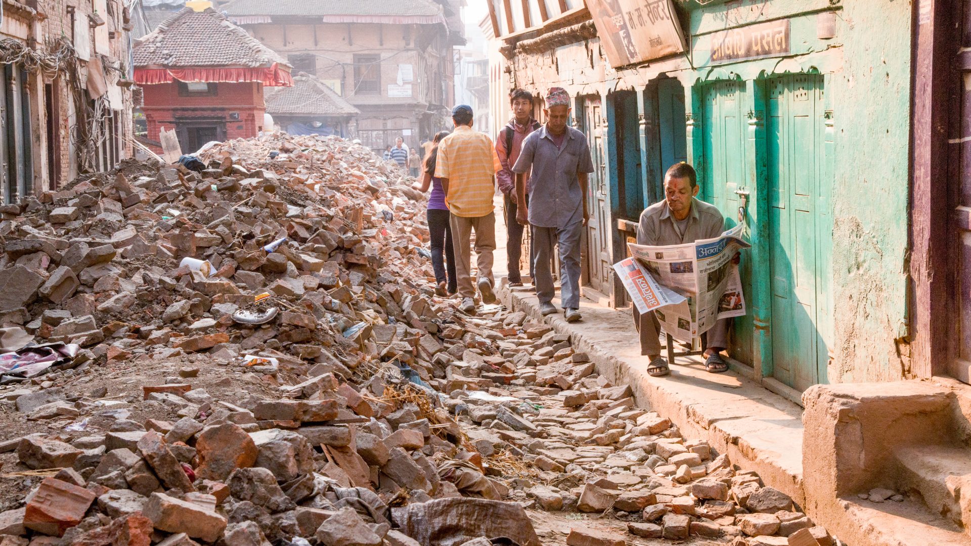 Man sits in front of his shop reading as life goes on around him after the Nepal earthquake in 2015.