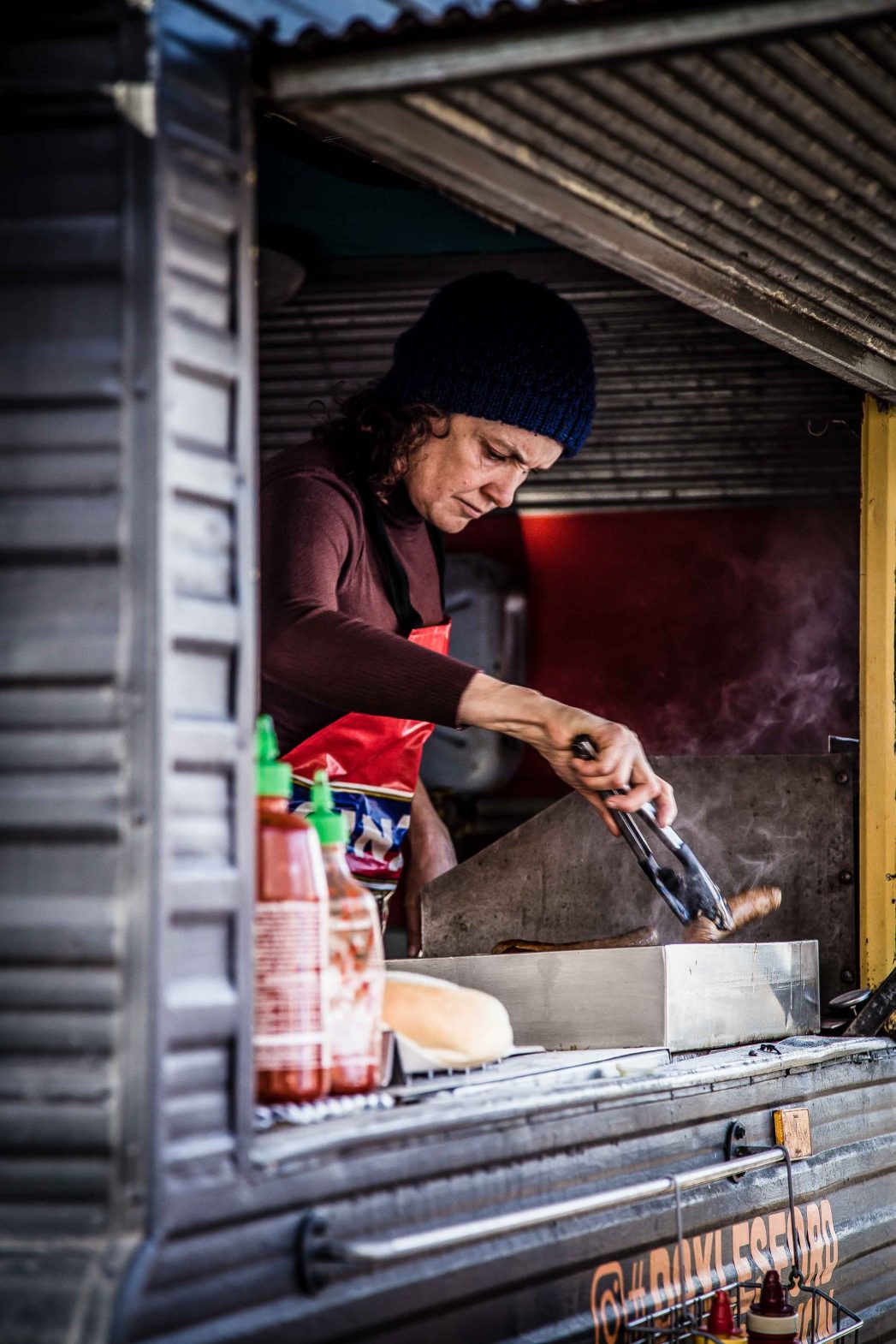 A woman grills meat from a food van.