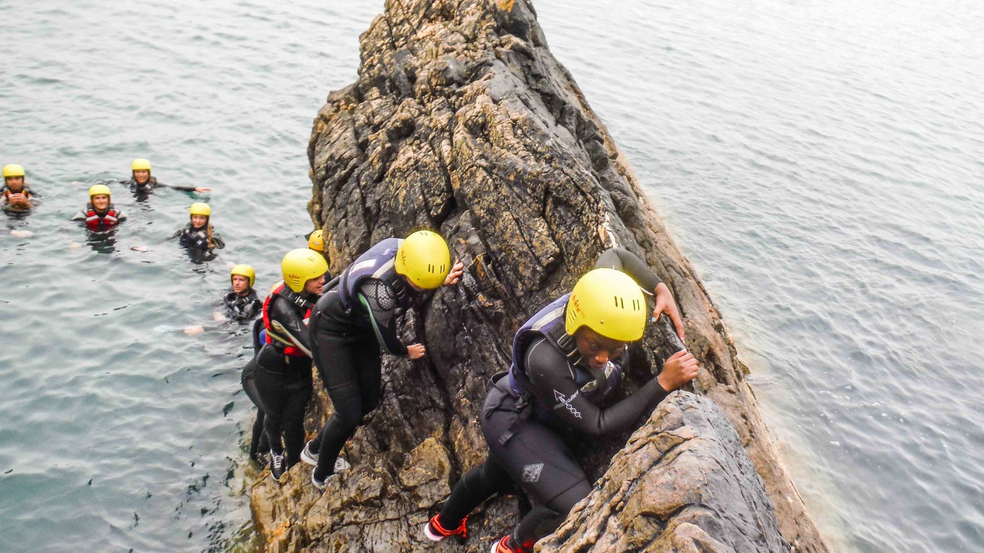 Clients make their way carefully up a rocky ledge on this coasteering adventure.