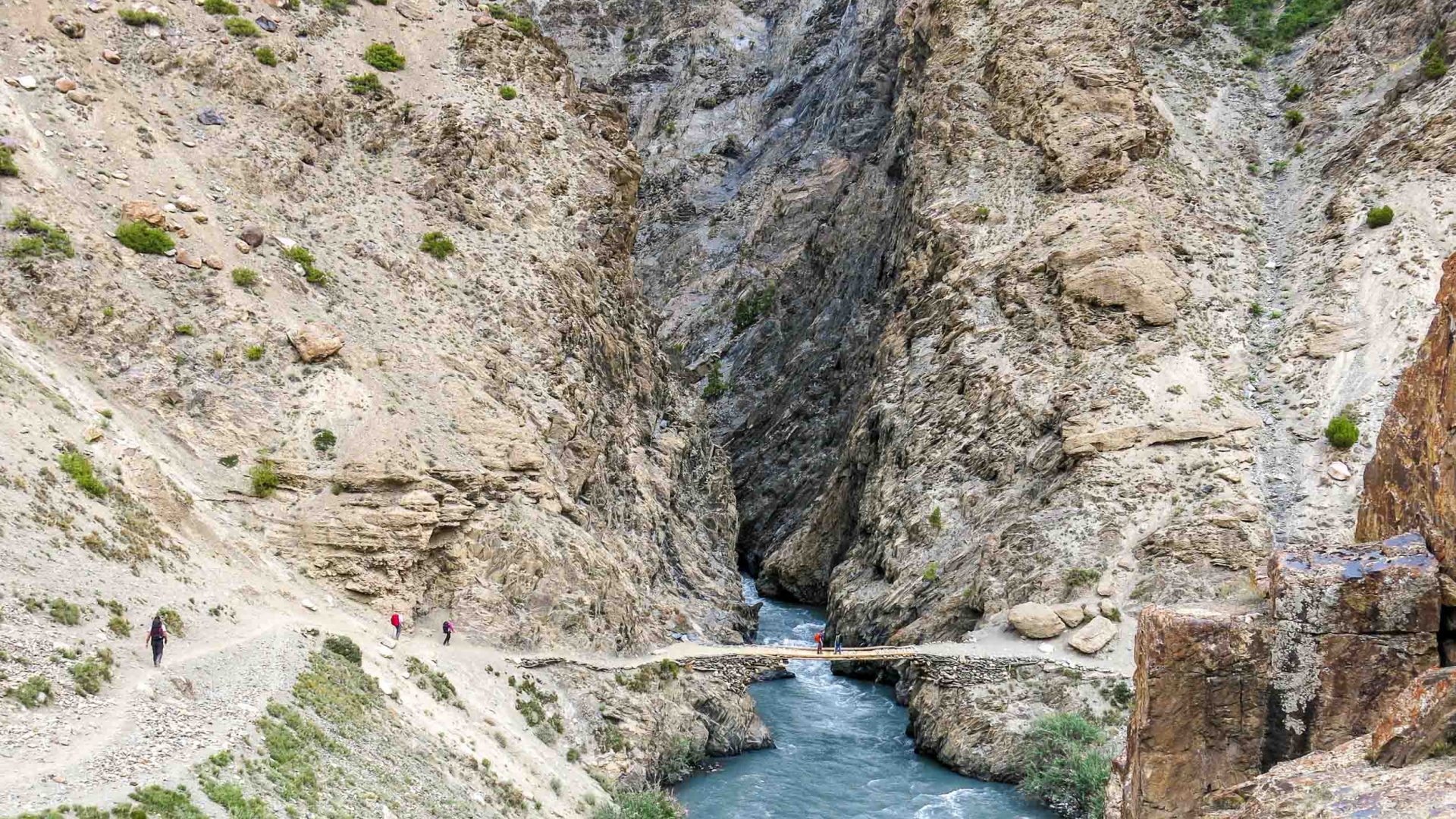 Travelers cross a narrow bridge as they trek through the arid mountains of the Wakhan.