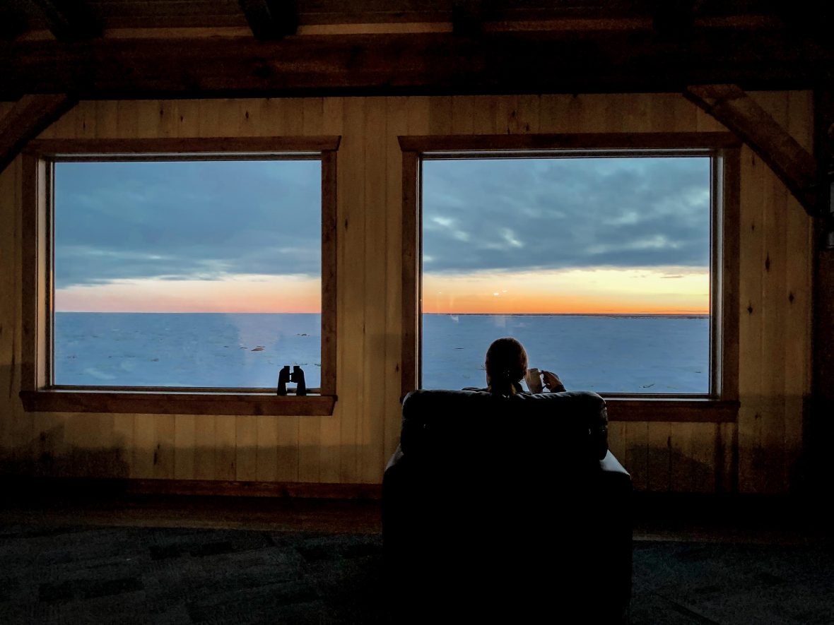 A guest relaxes with a mug of tea in the lounge while enjoying the sunset in Manitoba, Canada.