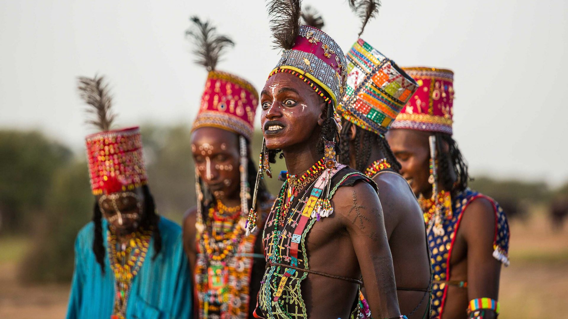 The Wodaabe men grimace during the dance to show off their white teeth. The ostrich feathers in their hats emphasizes their height.