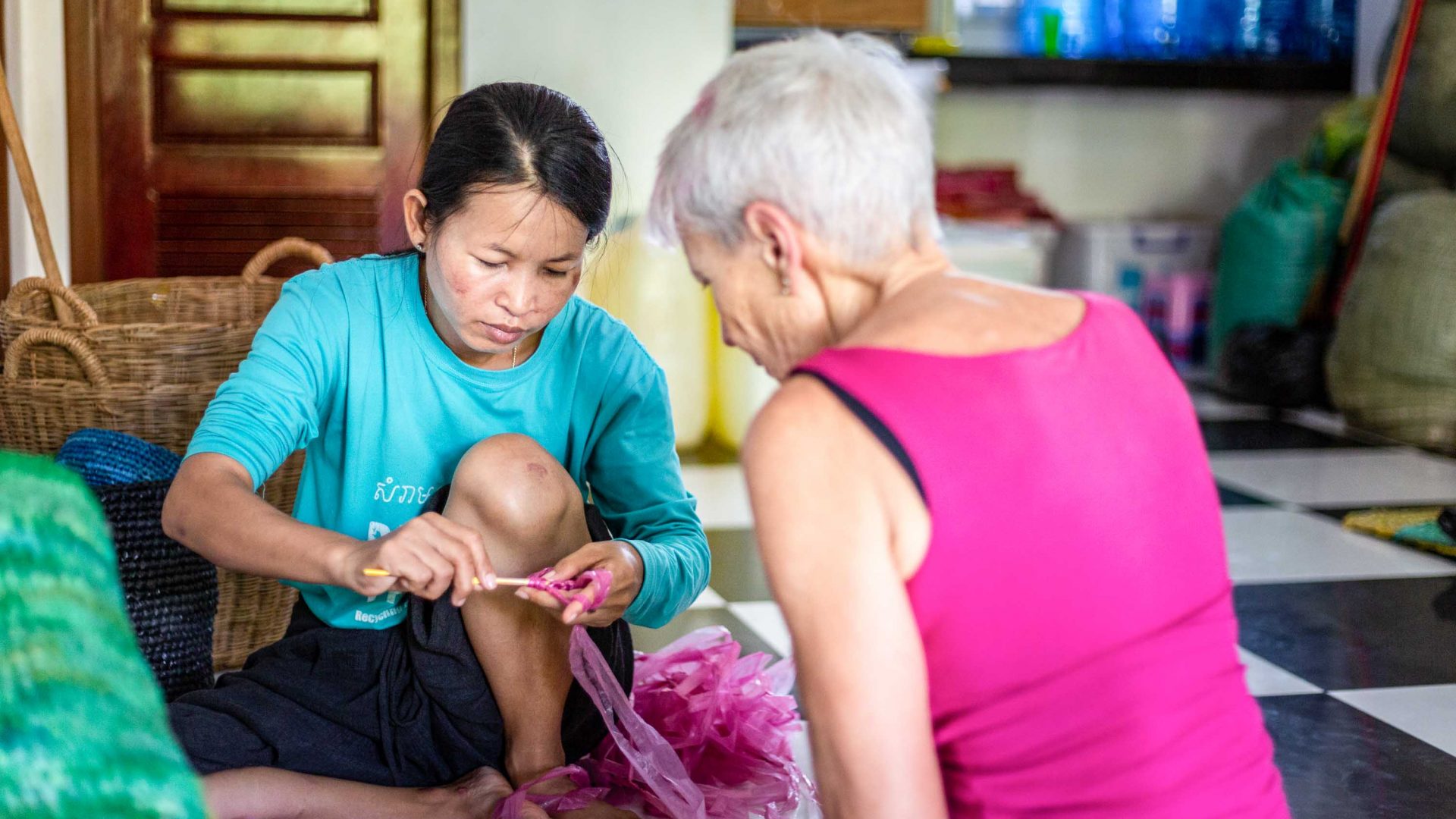 A woman from the Cambodian organization Rehash Trash shows a traveler the craft-making process.