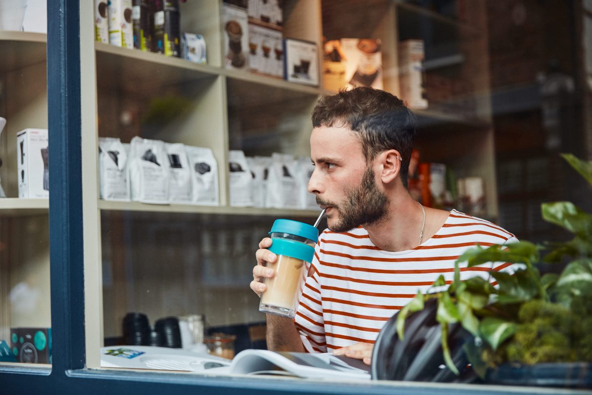 A man drinks out of a KeepCup in a cafe.