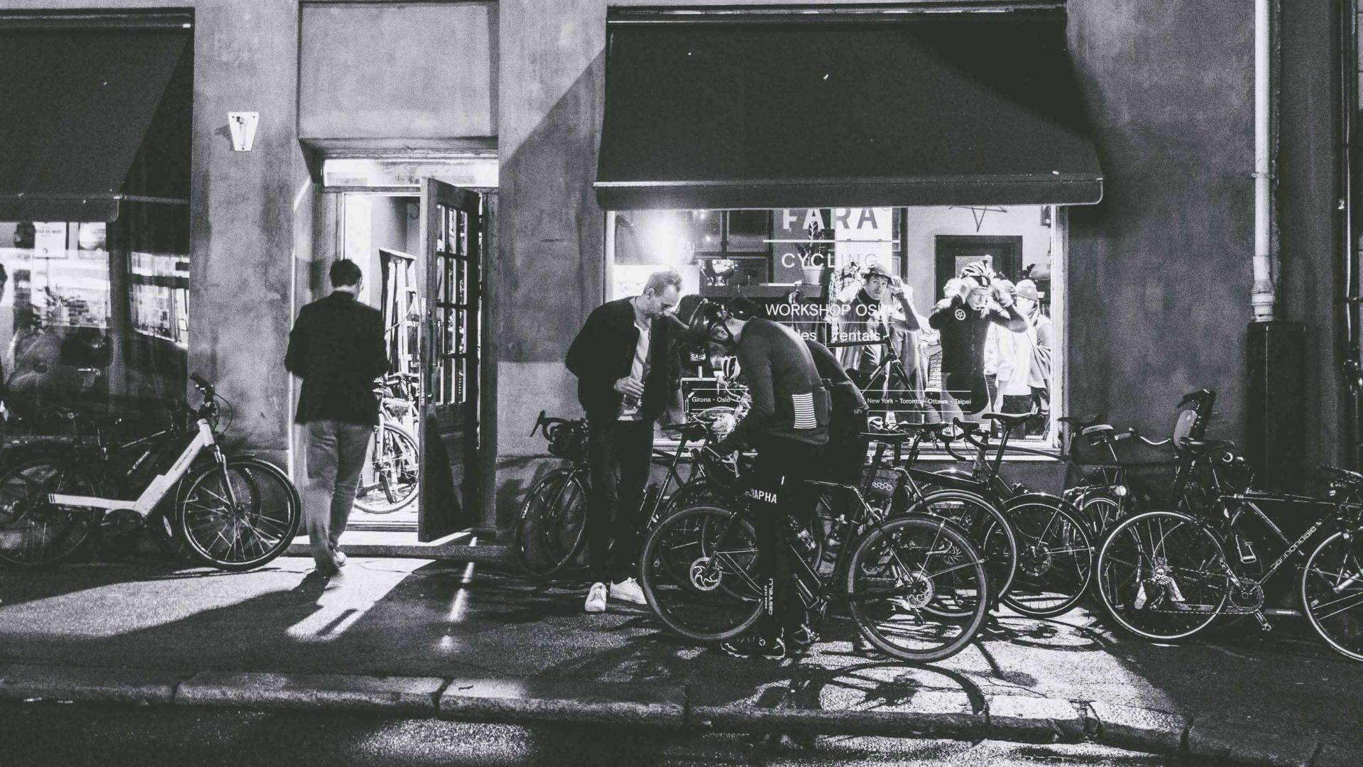 Bike riders work on their bikes outside a shop front.