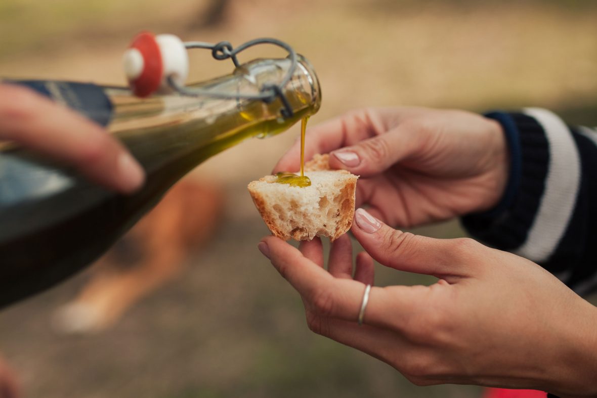 A person pours olive oil from a bottle onto a piece of bread.