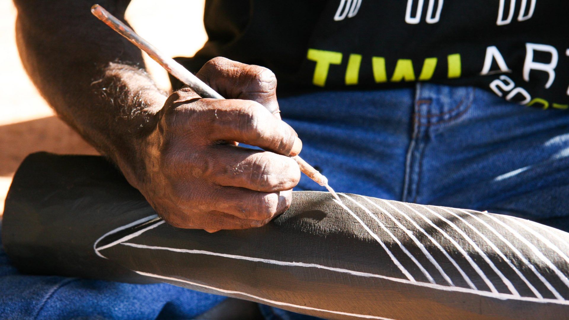 A man hands paints a cross hatch design.