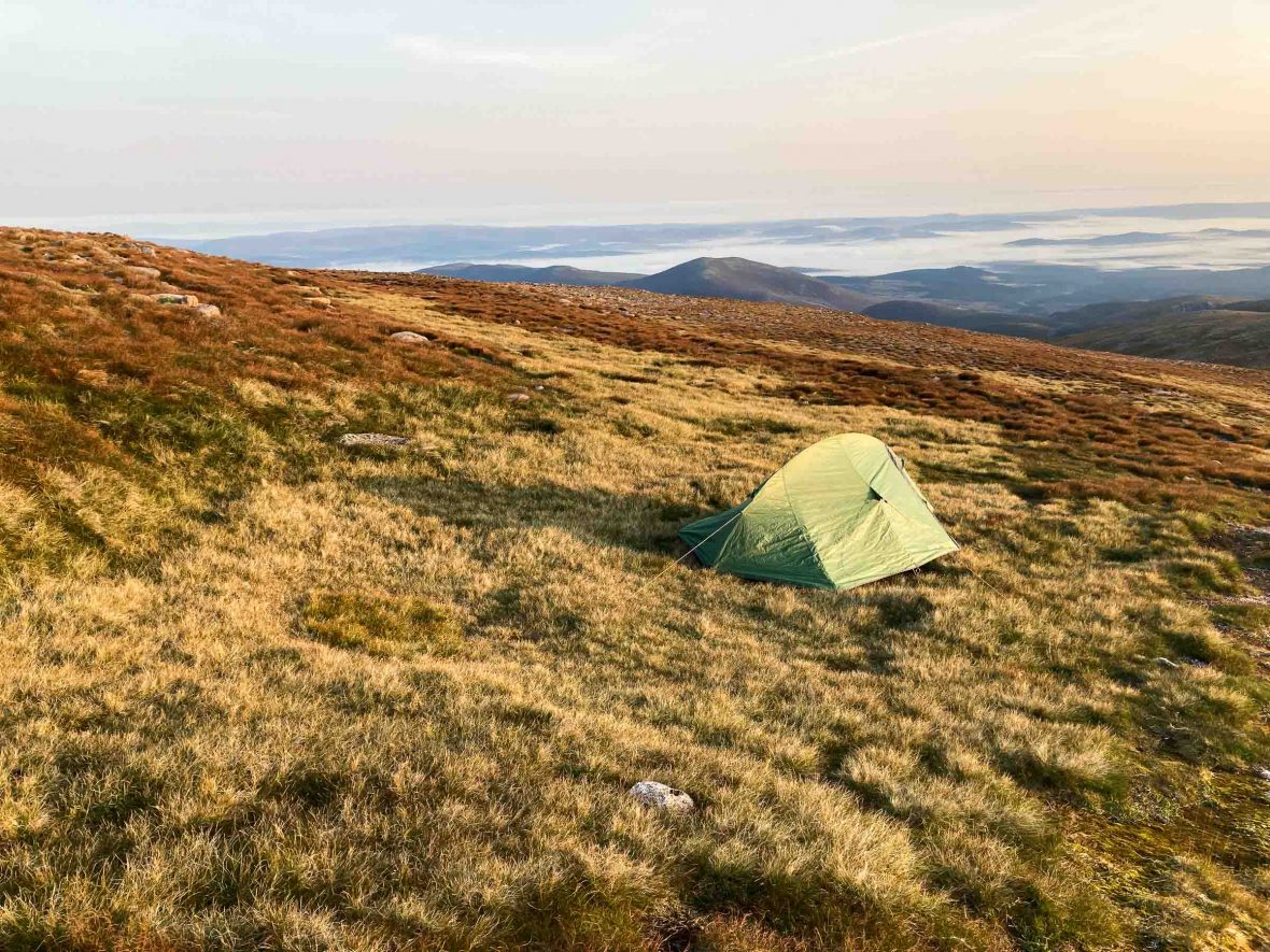 A green tent alone on a barren hill.
