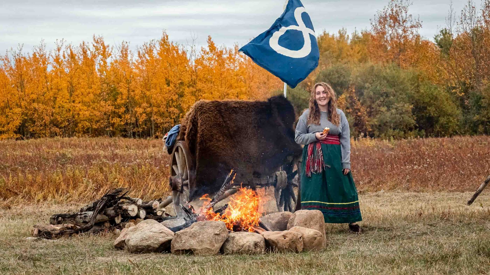 A woman stands beside a fire, with a flag behind her.