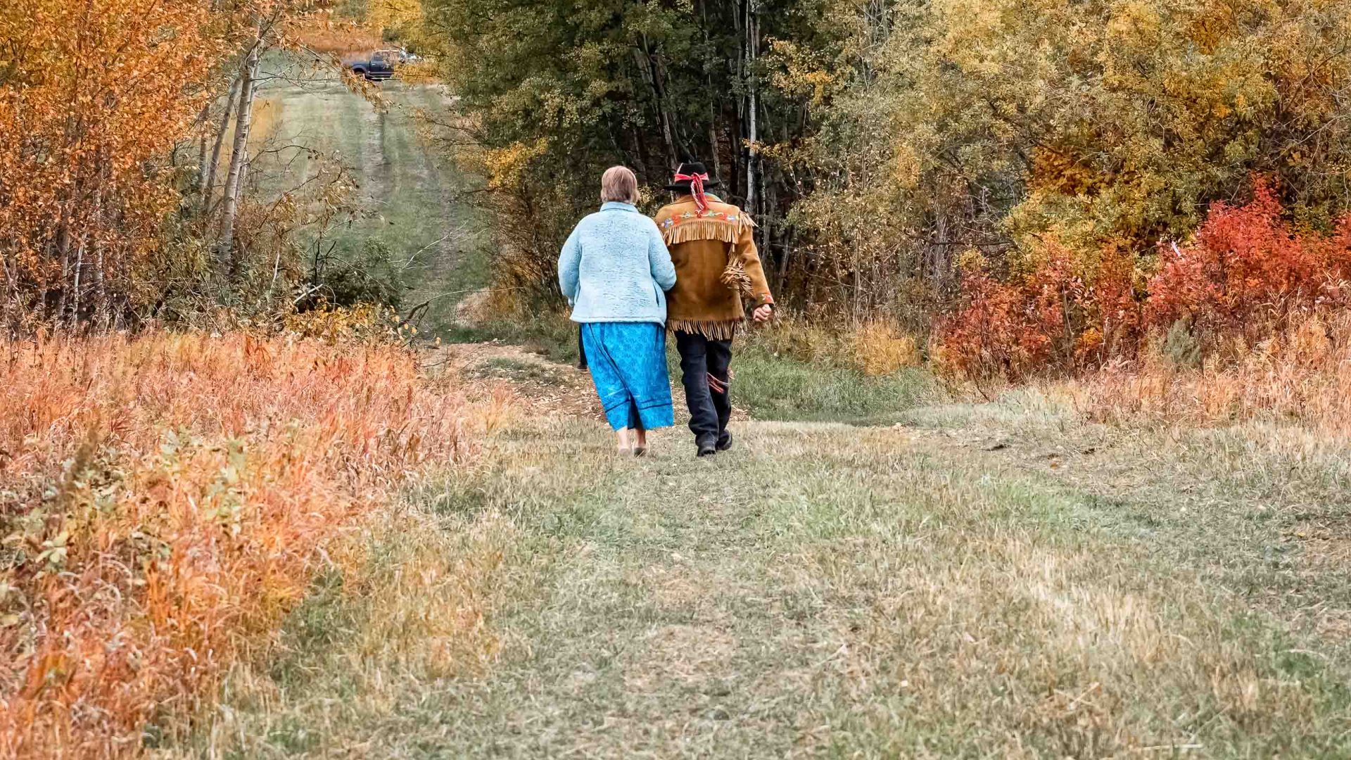 Two people walk across a grassy paddock.