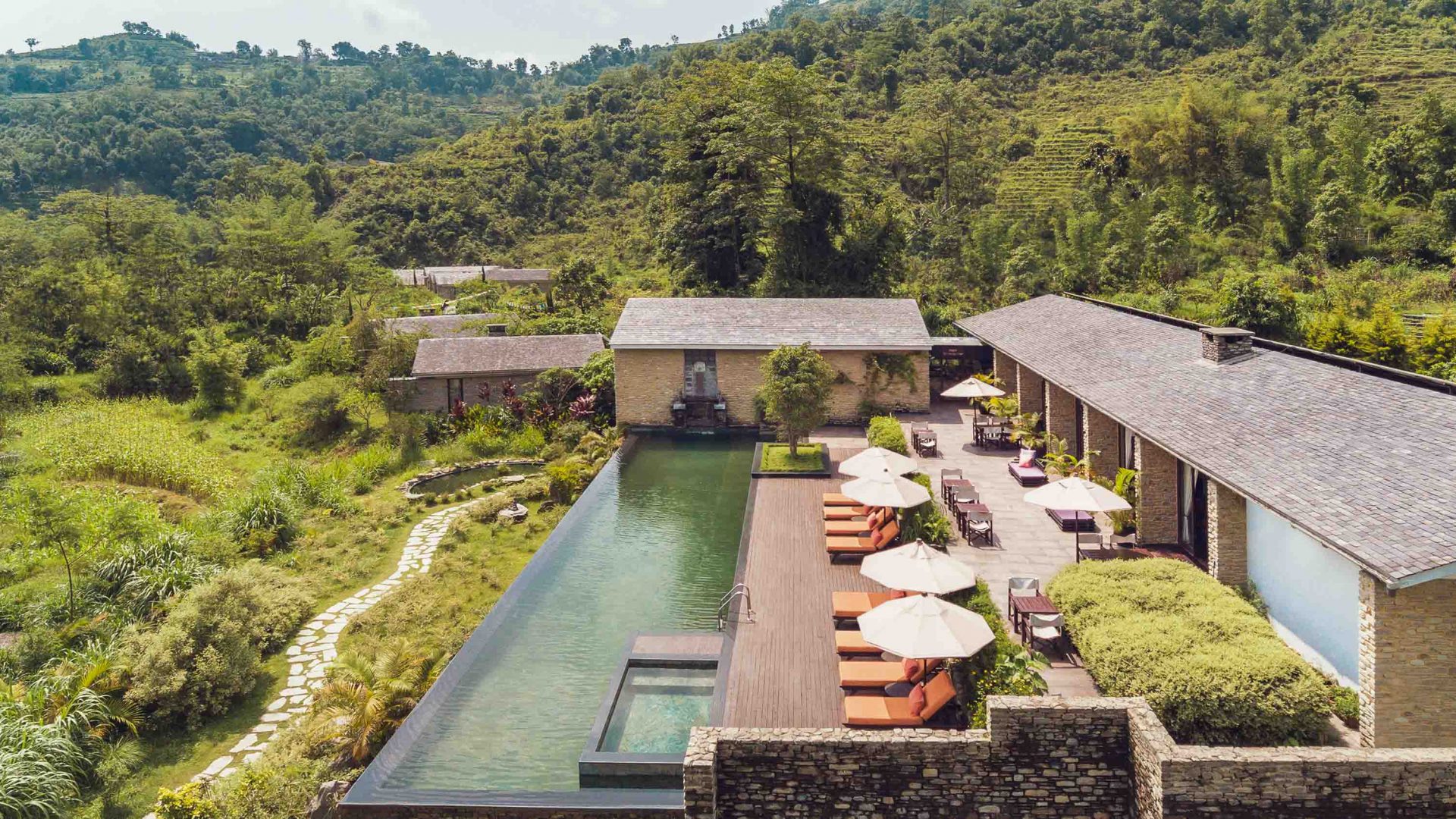 A hotel with a pool surrounded by green hills.