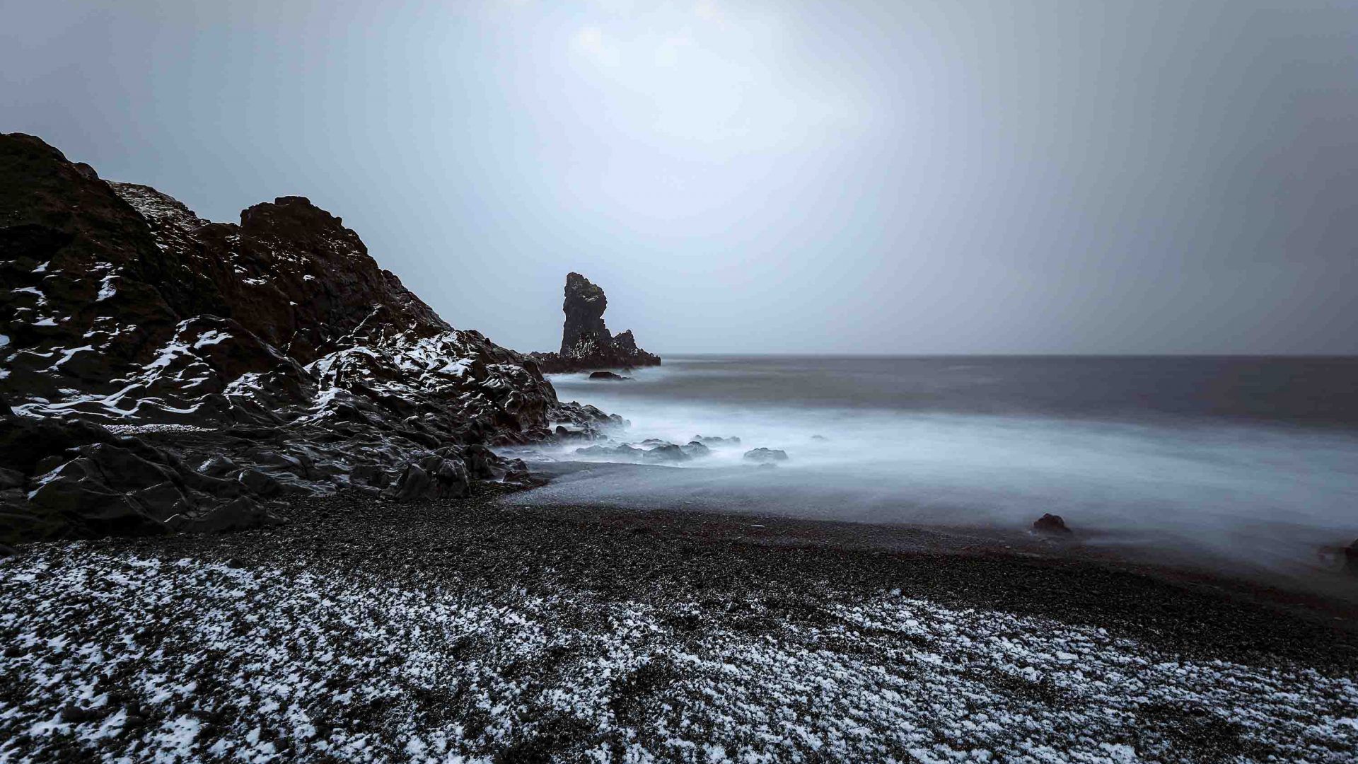 A moody scene of dark sky, cliffs and waters edge.