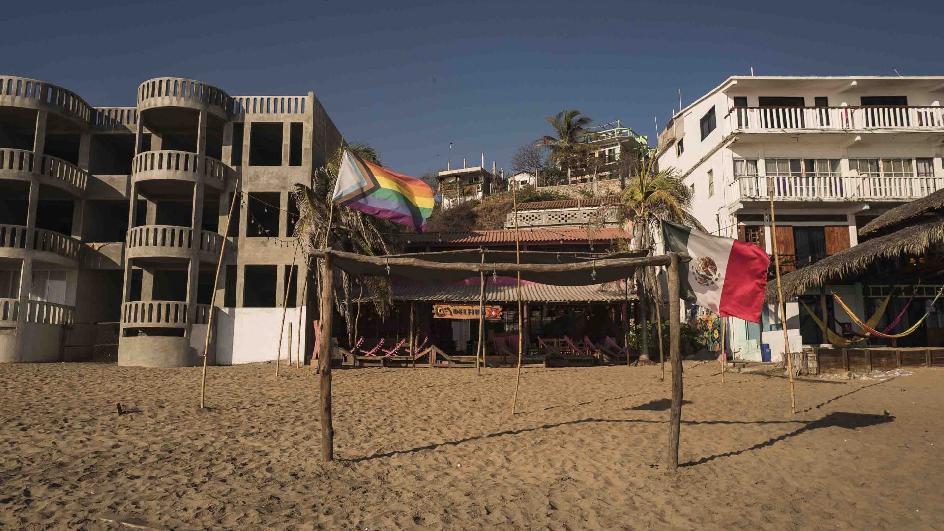 Buildings on the beach with a rainbow pride flag out front.