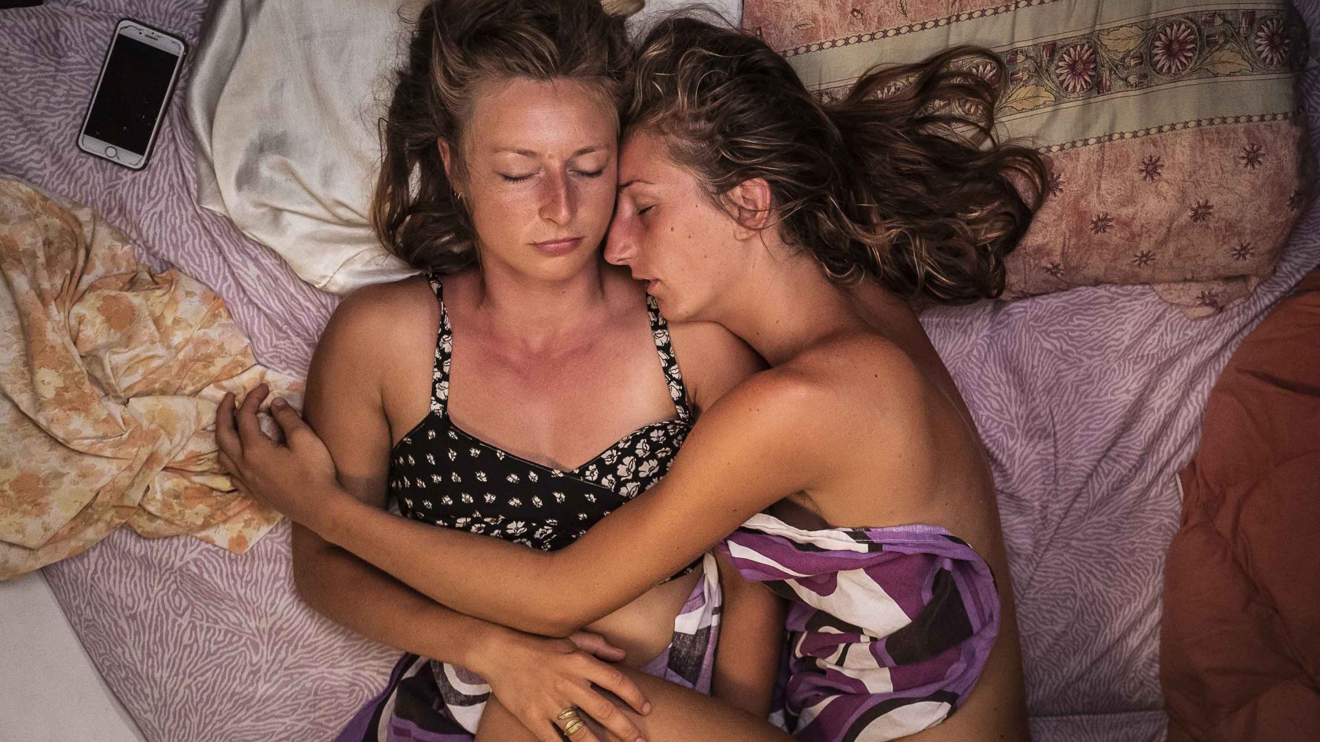Two women sleep embracing one another.