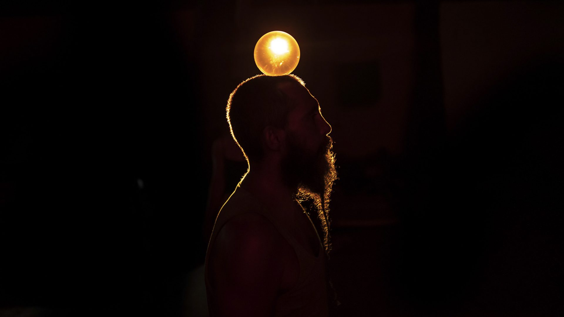 Stefano, silhouetted against the light, balances a glowing ball on his head.