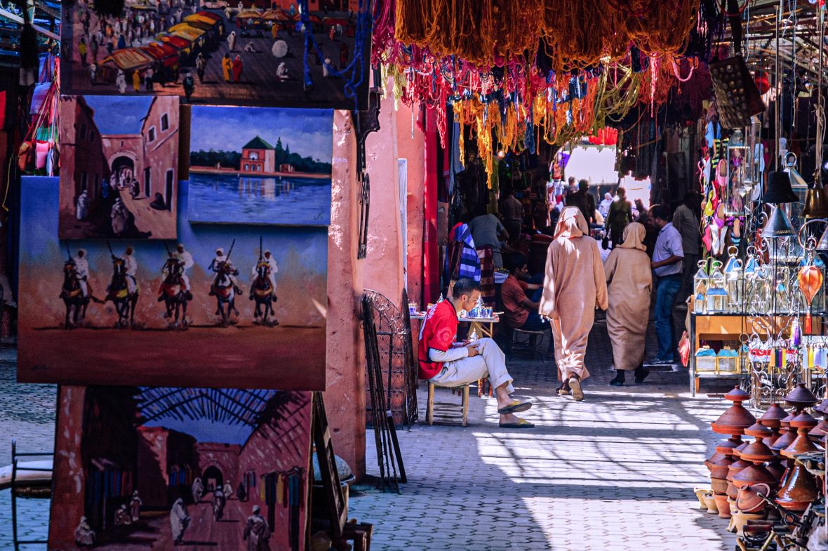 A painting in the foreground and backs of people walking through a market.