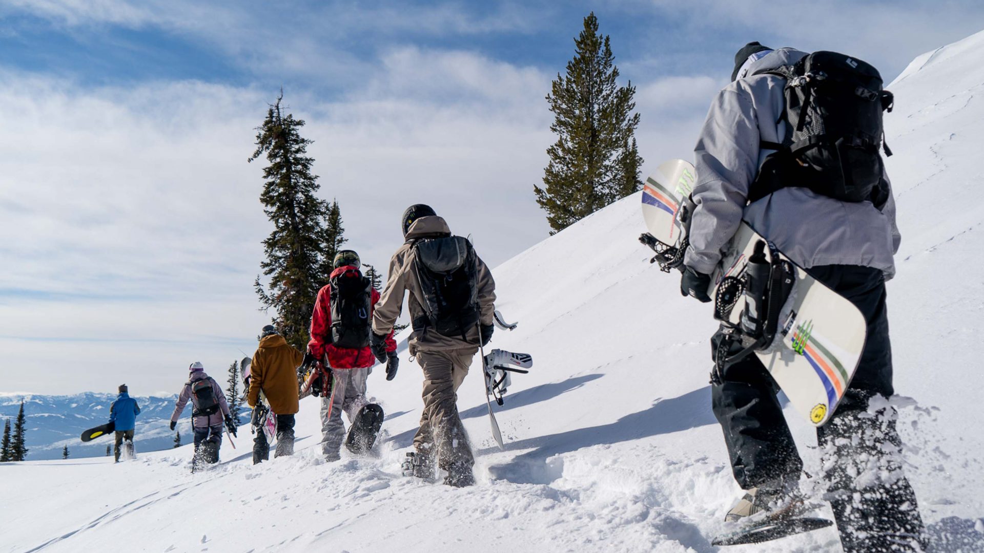 A single file of snowboarders traverses the mountain.
