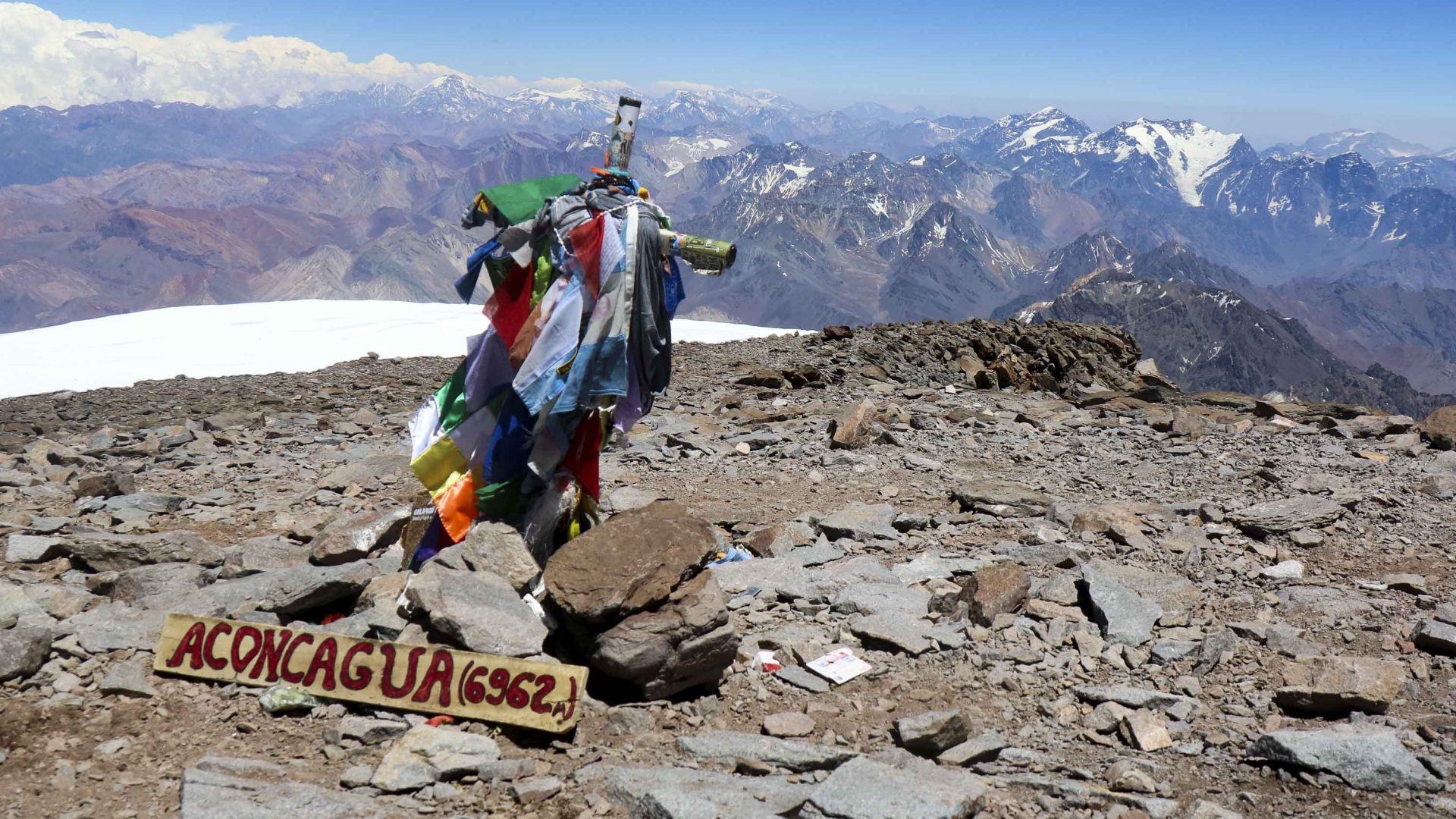 Prayer flags and a sign that reads 'Aconcagua' mark the summit of this mountain.