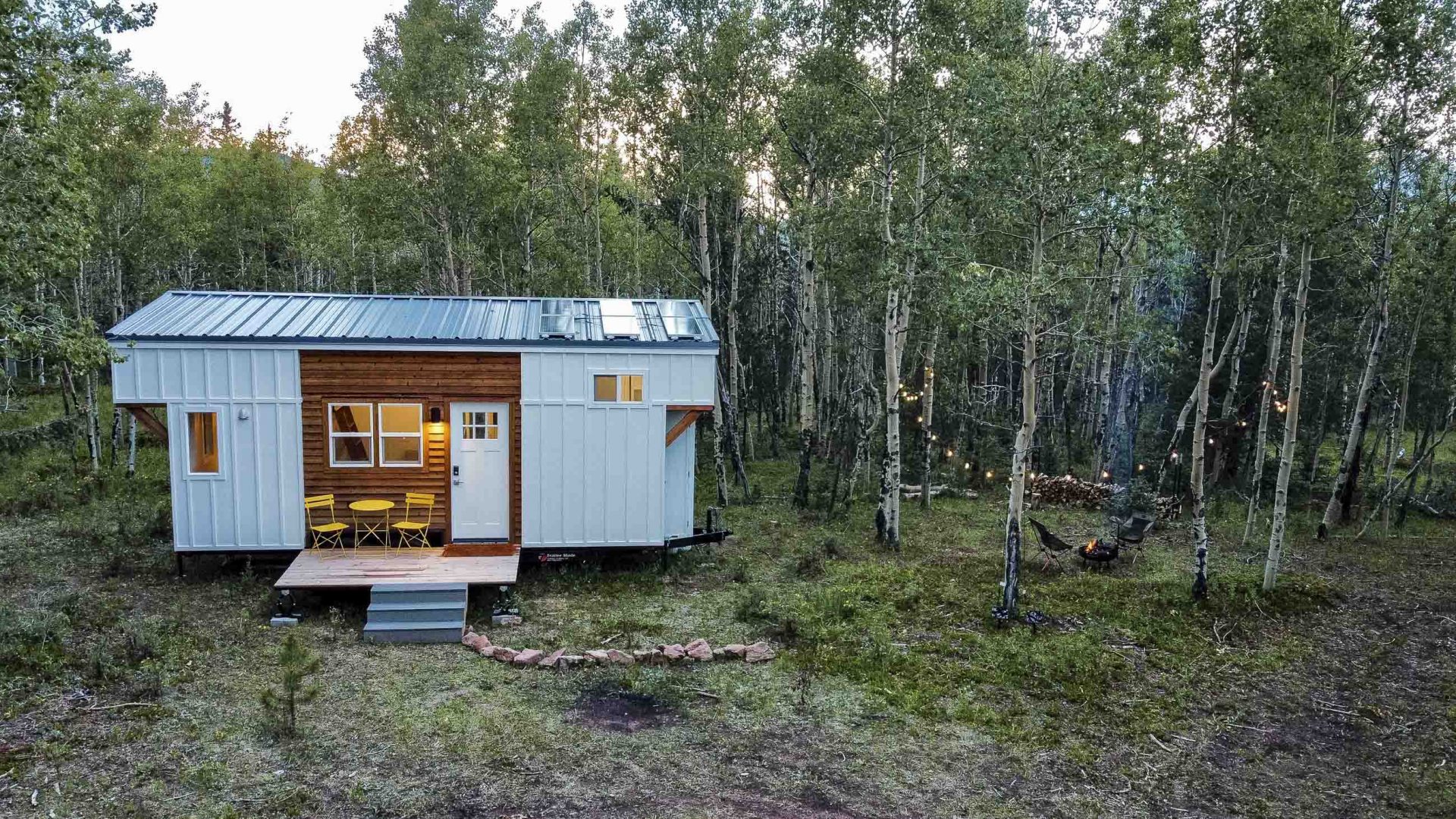 a tiny house lit up by soft lights stands in amongst trees.