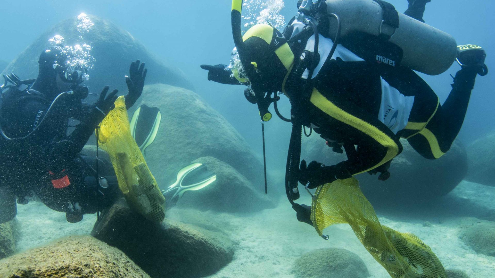 Divers work underwater looking for trash.