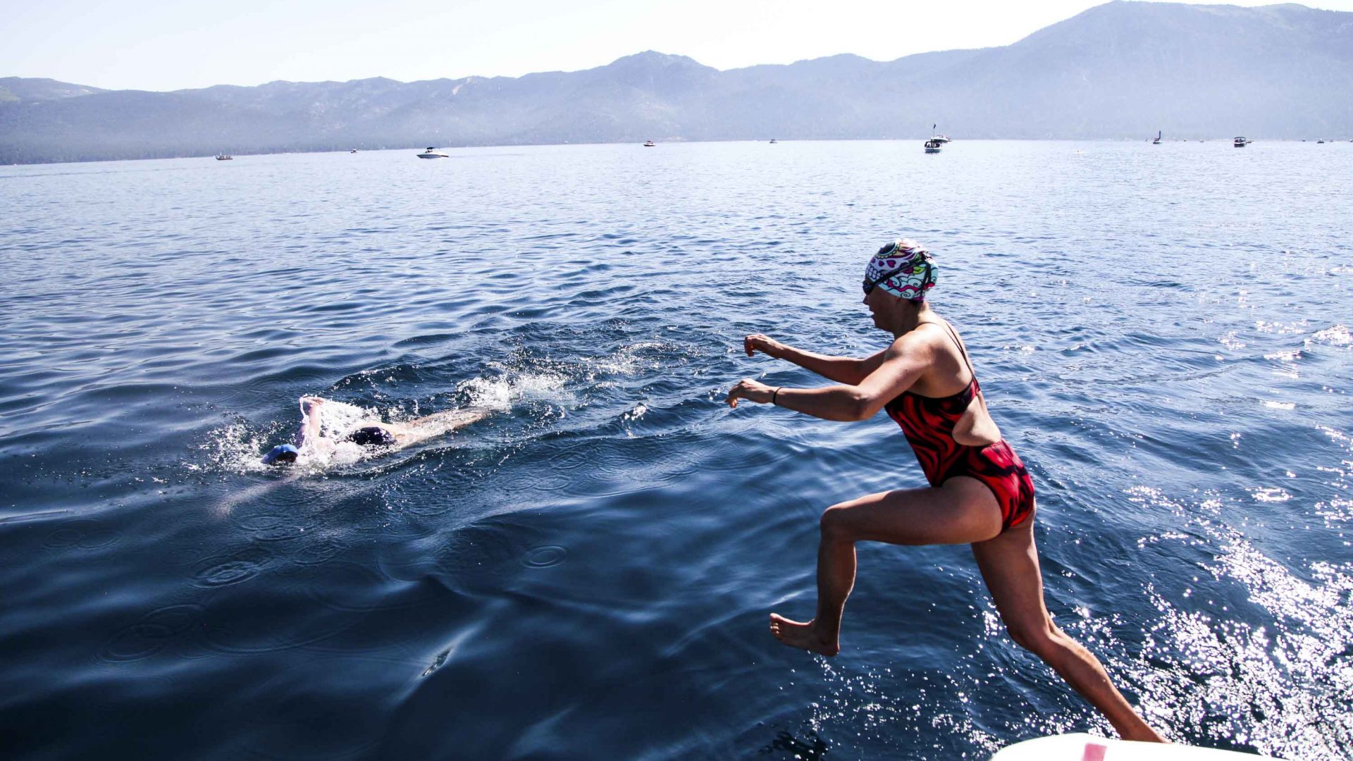 One woman jumps from a boat into the water while another swims by.