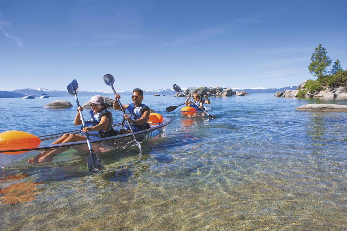 Three people kayak across the clear blue water of Lake Tahoe.