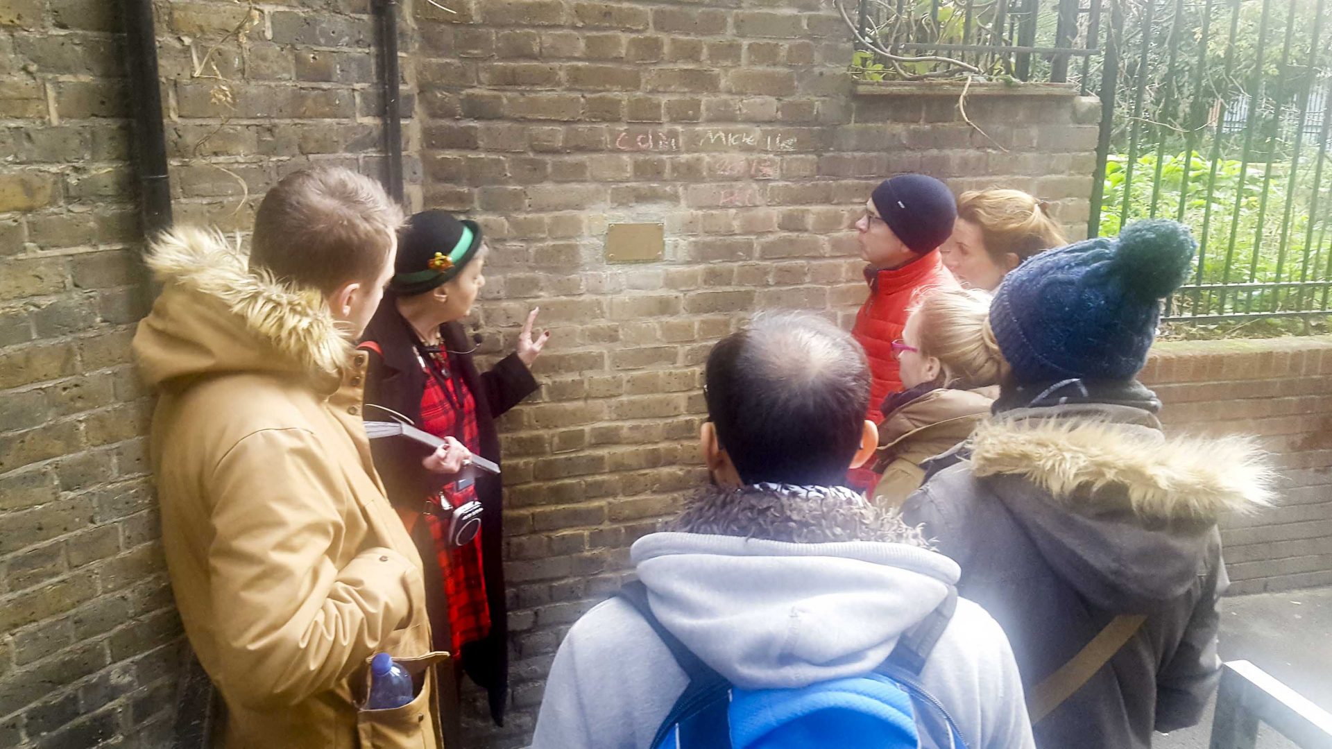A woman points to something on a brick wall to the tour group