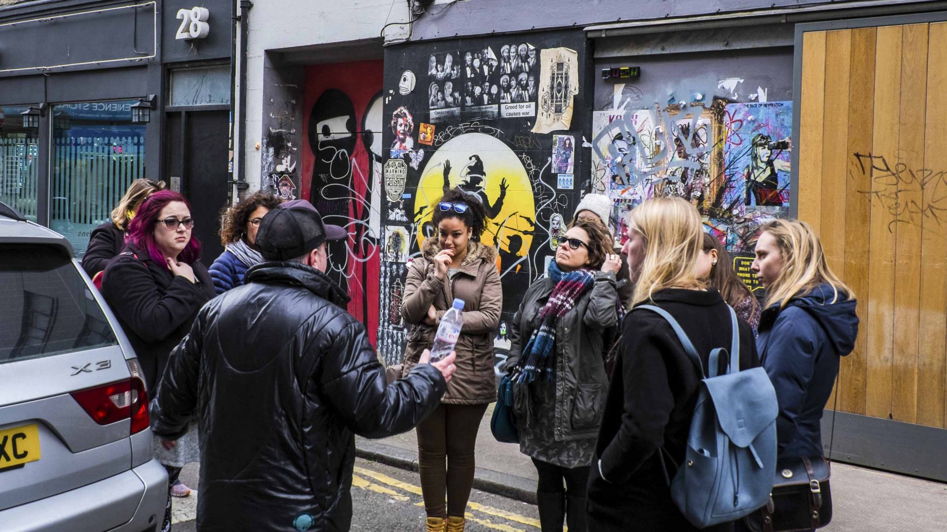 A man stands with a group of people from a tour in front of some street art.