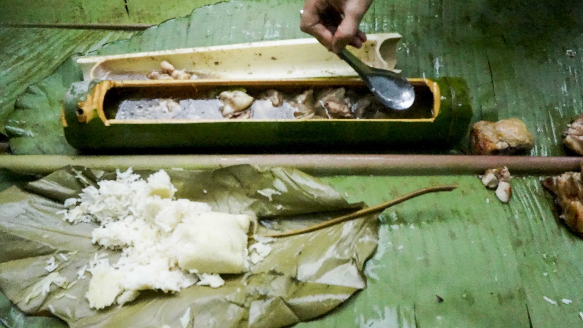 A meal of rice, meat and soup on some banana leaves. The soup is in a bowl made of bamboo.