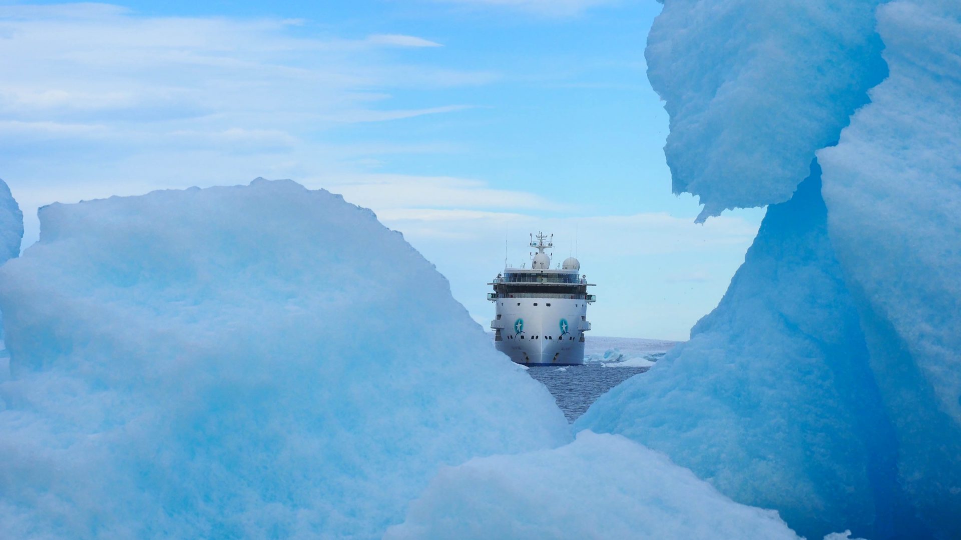 The Greg Mortimer ship can be seen through a gap in between icebergs.