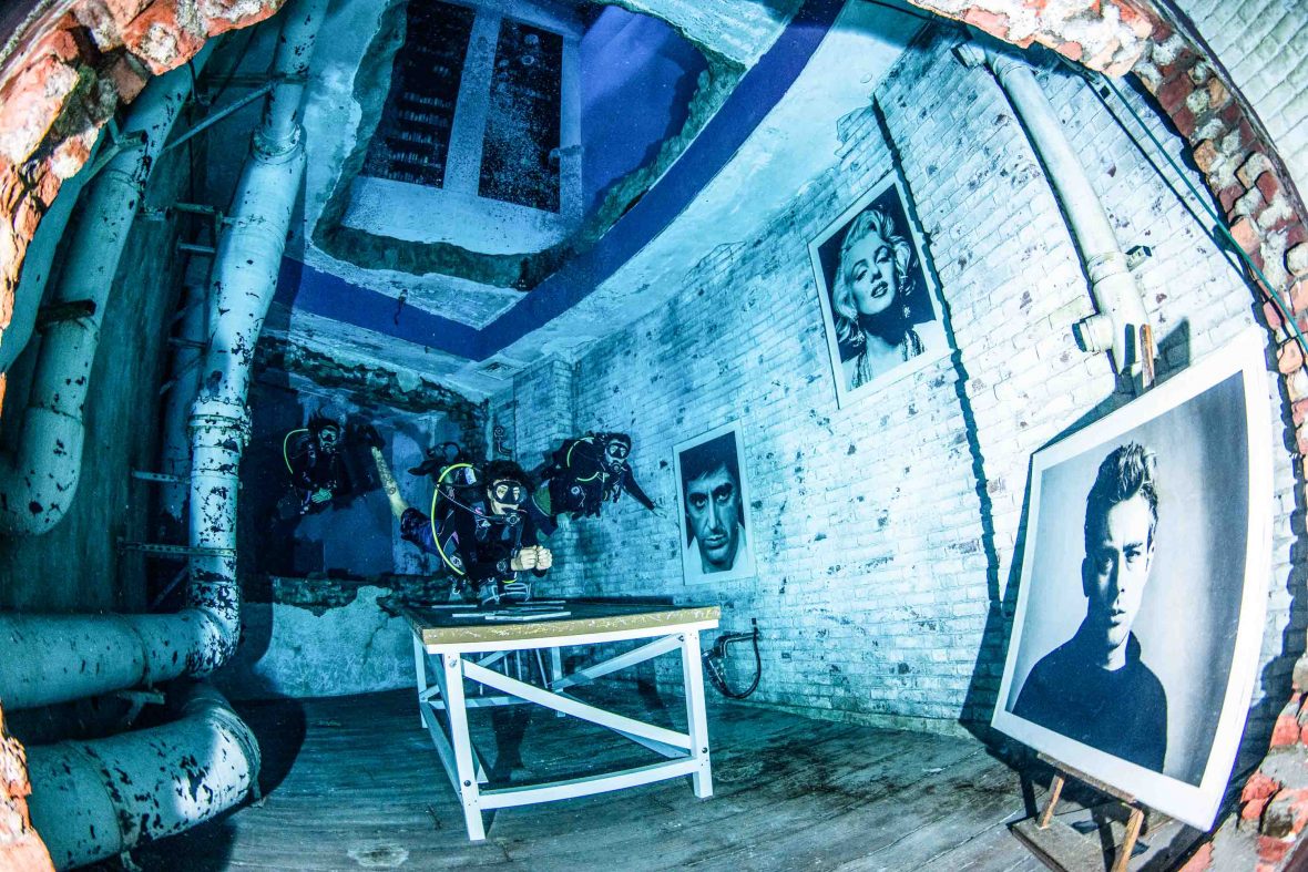 Divers swim through a room lined with pop art.