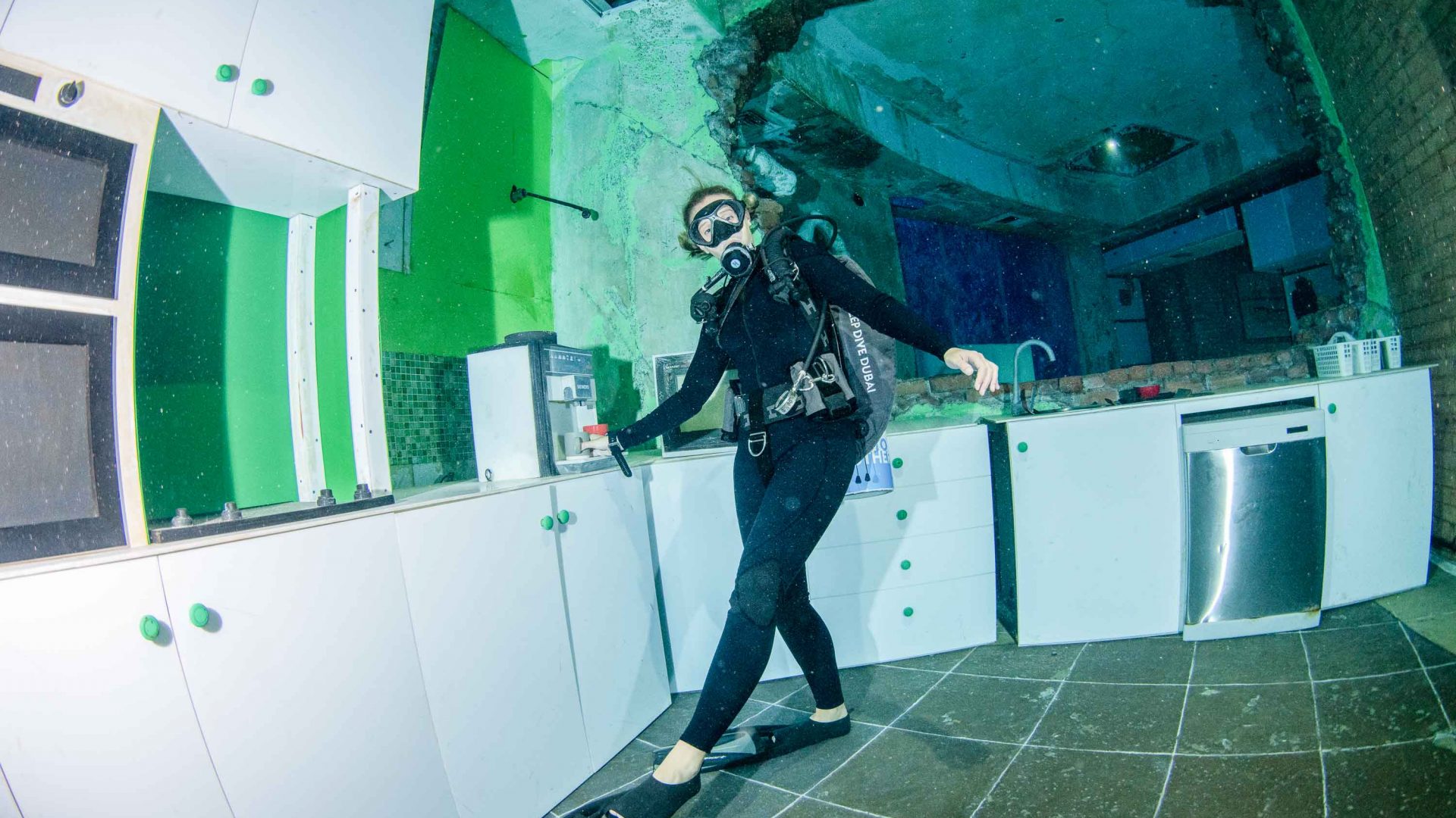 A diver leans against some cabinets in an underwater kitchen.