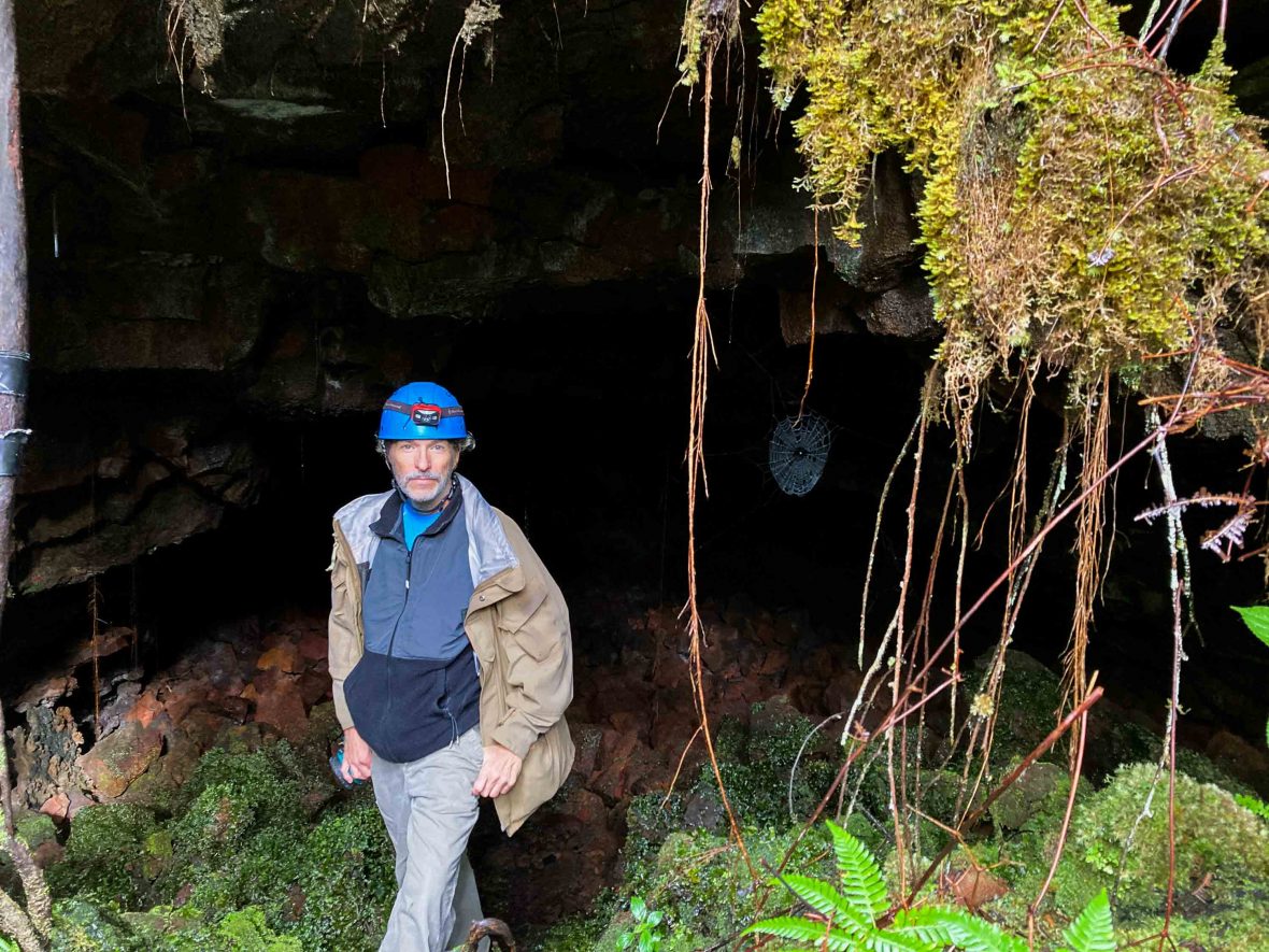 Harry stands in front of a cave wearing a hard hat.