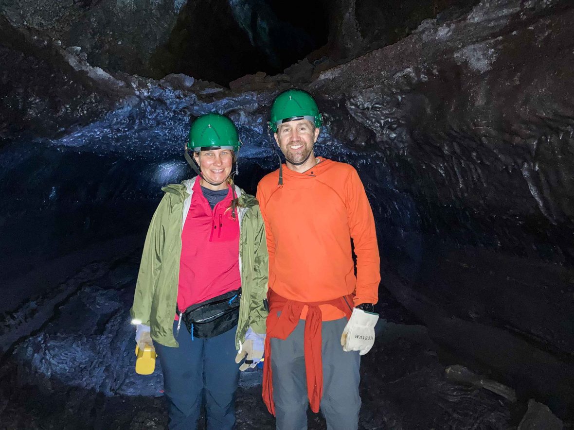Patrice and Justine smile in front of a cave wearing hard hats.