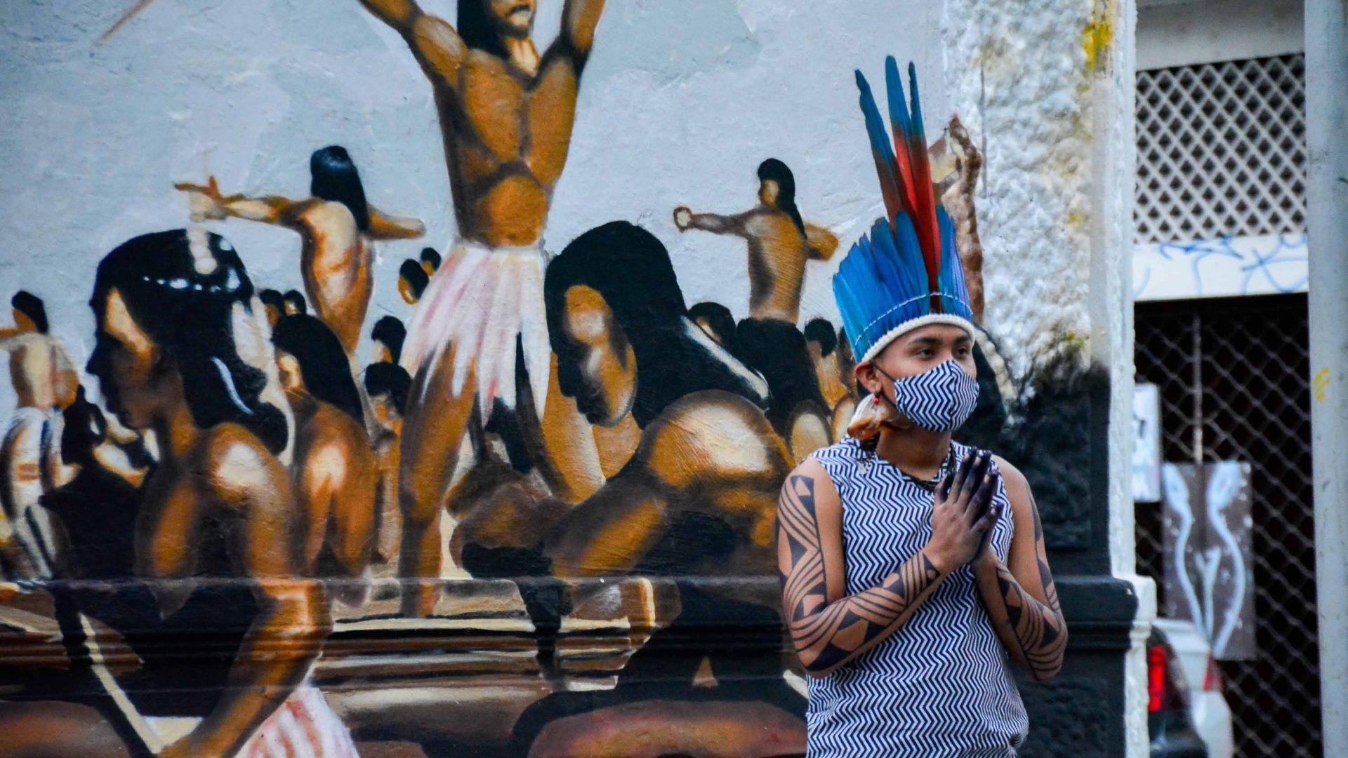 An indigenous person stands in front of a mural at the Indigenous Memorial.
