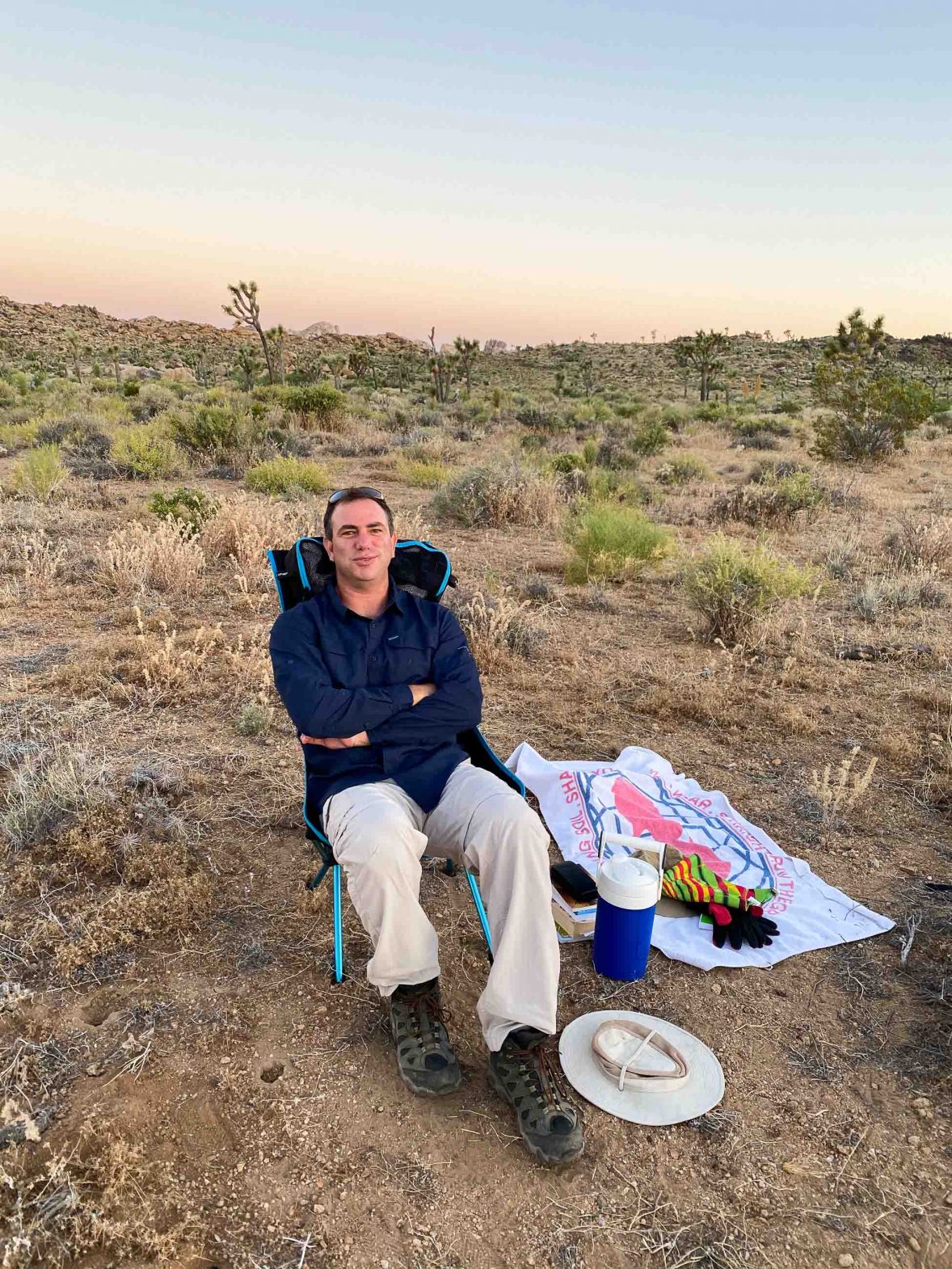 Robby sits in dru terrain with a blanket beside him with some snacks on it.