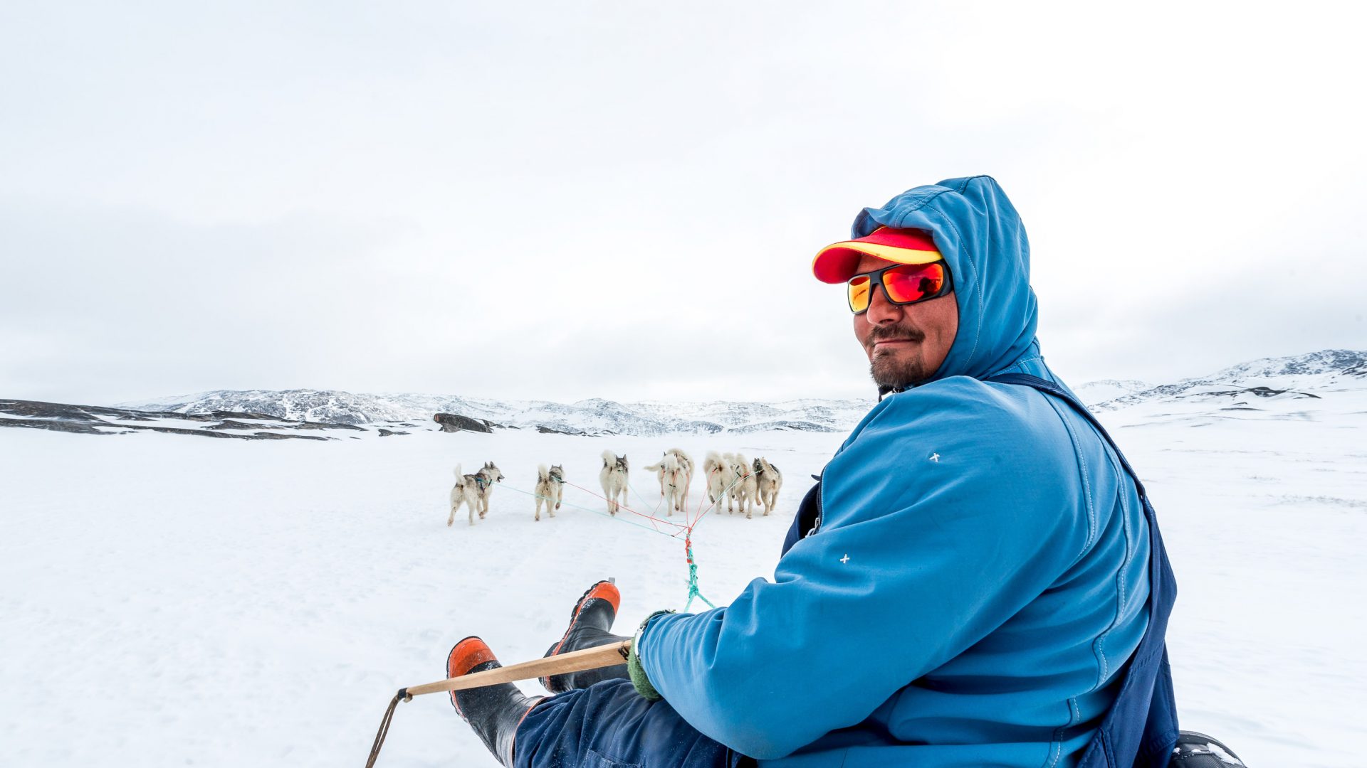 A man smiles while riding a dog sled.